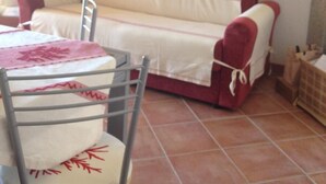 Un salon avec un canapé, une table à manger entourée de chaises, un tableau encadré au mur et un sol carrelé.