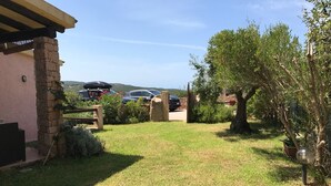 Une cour verdoyante avec un mur de pierre, une clôture en bois et une voiture garée.