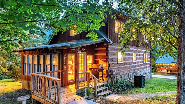 Een houten blokhut met een veranda, een barbecue en een pad van stenen.