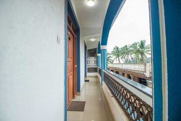 A corridor with a wooden door, a balcony with a metal railing, and a view of palm trees. - Baga Beach Myron (Baga)