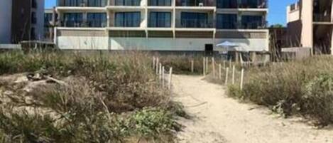 A multi-story hotel with a central courtyard and a sandy path leading to the entrance.