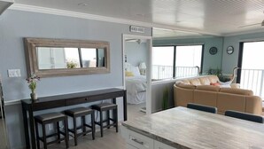 A modern kitchen with a marble countertop, a dining area with a dark wooden table and stools, a beige sofa in the living area, and a sign indicating a beach house. - Beachfront Penthouse, private rooftop balcony & jacuzzi (South Padre Island)