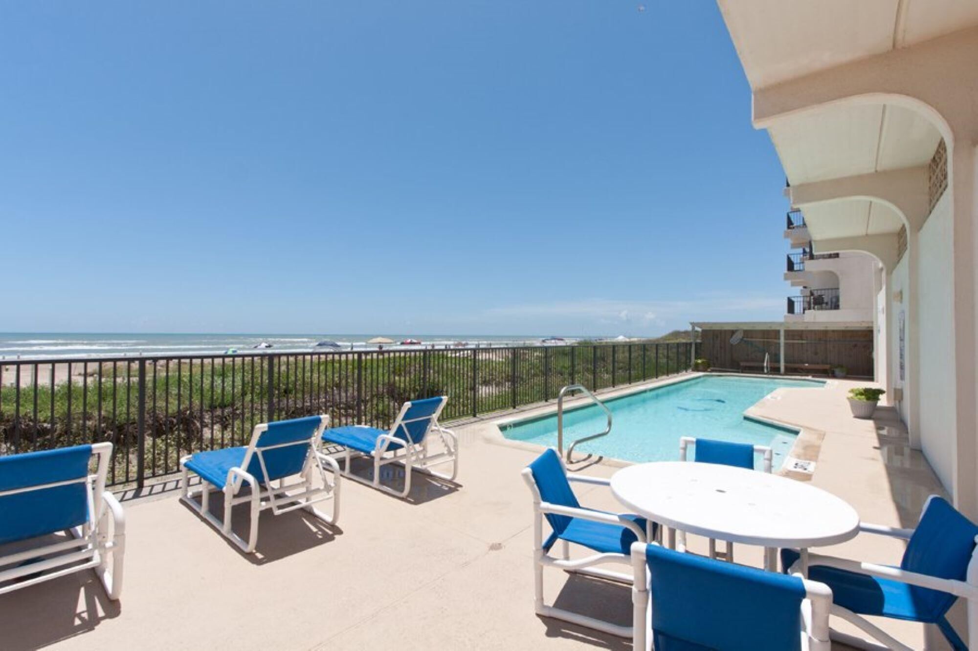 A balcony with a pool, blue chairs, and a table.