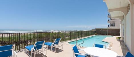 A balcony with a pool, blue chairs, and a table.