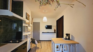 Une cuisine compacte comprenant une cuisinière, une table à manger avec des tabourets, un téléviseur fixé au mur et une branche décorative suspendue au plafond.
