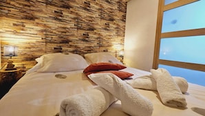 Une chambre d’hôtel avec un mur en bois, un lit avec des oreillers blancs et rouges, et une fenêtre donnant sur un paysage.