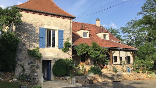 Un bâtiment en pierre avec un toit recouvert de tuiles rouges, un petit balcon et un escalier en pierre menant à une porte.