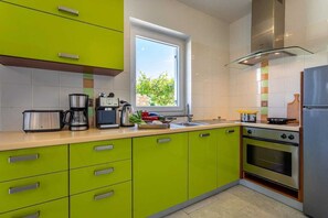 Cozinha moderna com armários verdes, fogão de aço inoxidável, janela com vista e forno embutido.