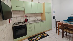 A kitchen with a gas stove, oven, sink, and green cabinets. There is a dining table with chairs and a black placemat with fruit designs. - Holiday Home "Casa Barbara" with Air Conditioning and WiFi (Nebida)