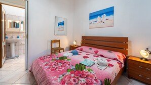 A bedroom with a bed, a nightstand, a chair, a painting, and a bathroom visible through an open door. - Holiday Home "Casa Barbara" with Air Conditioning and WiFi (Nebida)
