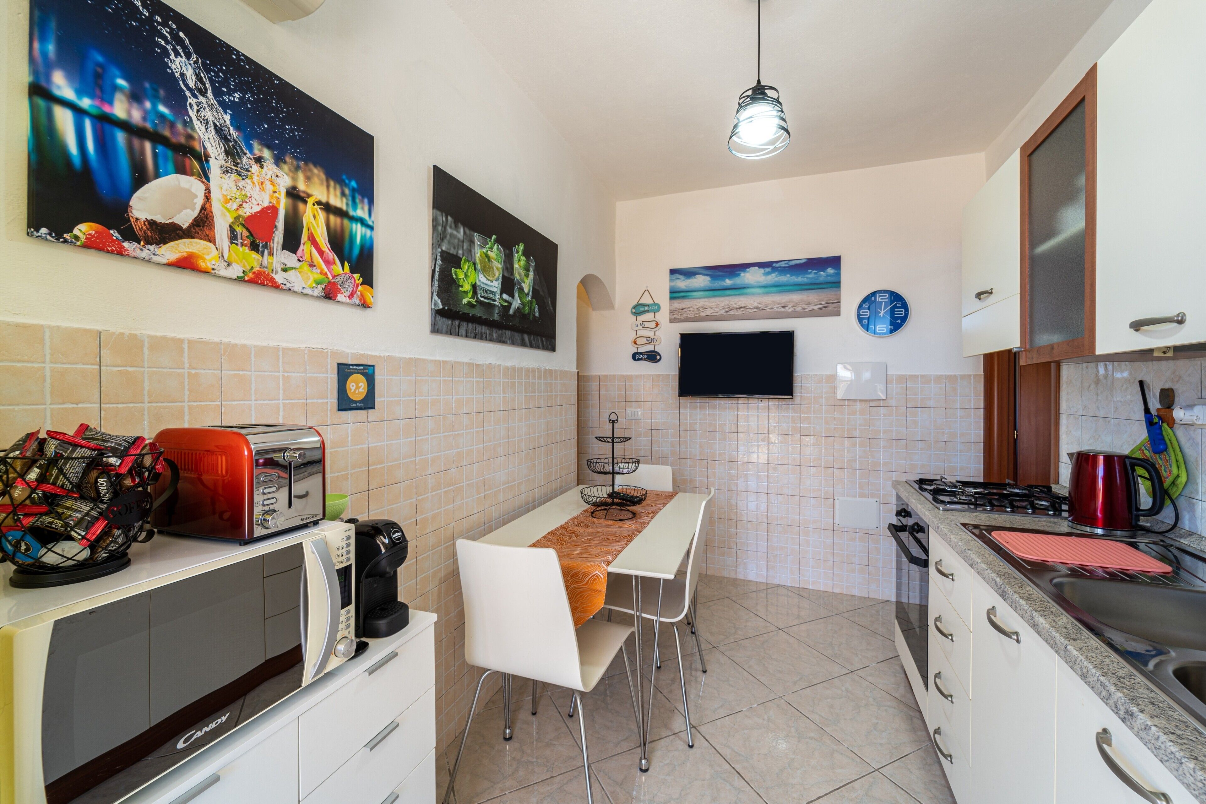 Une cuisine compacte équipée d’un four à micro-ondes, d’un grille-pain et d’un évier. On y trouve également une table à manger avec des chaises et un téléviseur fixé au mur.