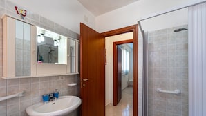 Ein Badezimmer mit Waschbecken, Spiegel, Dusche und einer Tür zu einem anderen Raum.