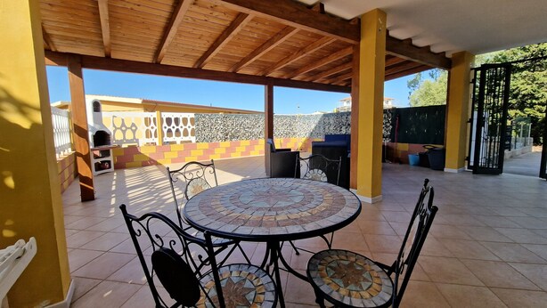 Eine Terrasse im Freien mit einem runden Tisch und Stühlen, einer Holzbeschichtung und Blick auf ein Gebäude im Hintergrund.