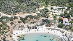 Eine Küstenlandschaft mit sandigem Strand, klarem türkisblauem Wasser und einer Felsformation mit antiken Ruinen.
