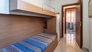 Ein Stockbett mit einem hölzernen Kopfteil und einem Bett darunter. Eine Tür führt zu einem Badezimmer mit Toilette und Waschbecken.