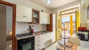 Eine moderne Küche mit Gasherd, Backofen und weißen Schränken. Ein Essbereich mit Tisch und Stühlen, sowie ein Fenster mit Blick nach außen.