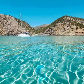 Een heldere turquoise zee met een zeilboot afgemeerd nabij rotsachtige heuvels.