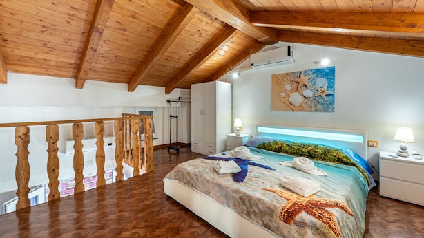 Un dormitorio con techo de madera, una cama con diseño de estrella de mar, una mesita de noche y una lámpara de pared.