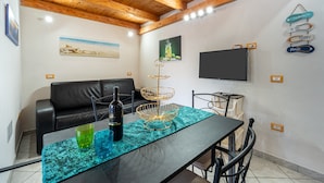 Una sala de estar moderna con un sofá de cuero negro, una mesa de comedor con un mantel individual verde azulado, una botella de vino y copas.