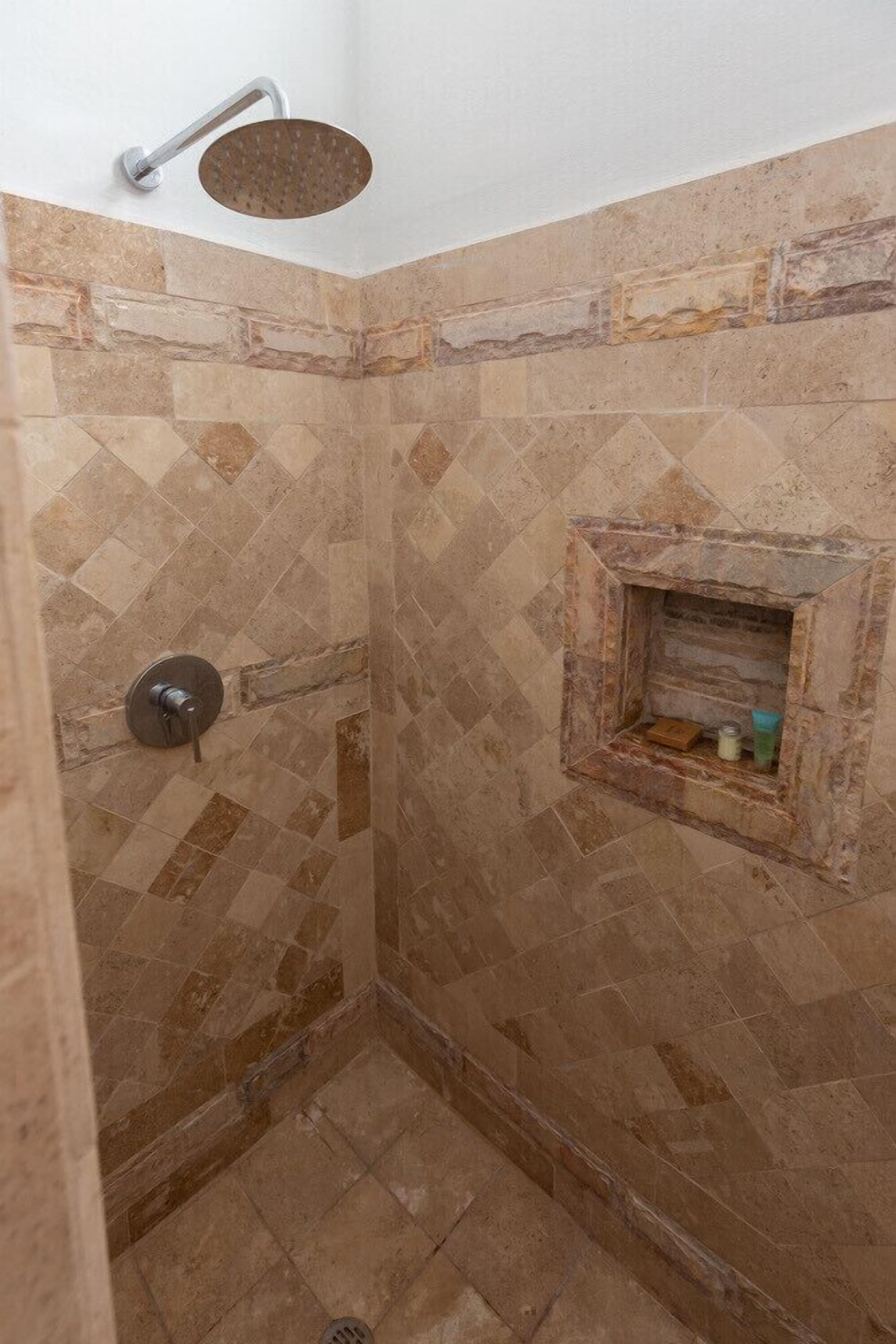 Een douche met een handdouche en een ingebouwd plankje met toiletartikelen.