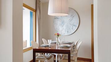 Een eetruimte met een houten tafel, witte stoelen, een hanglamp en een groot abstract schilderij aan de muur.