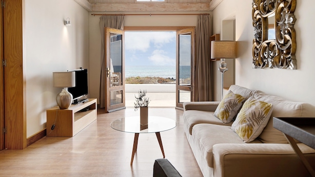Un salón con televisor, una mesa de centro, un sofá y vista al mar a través de puertas abiertas.