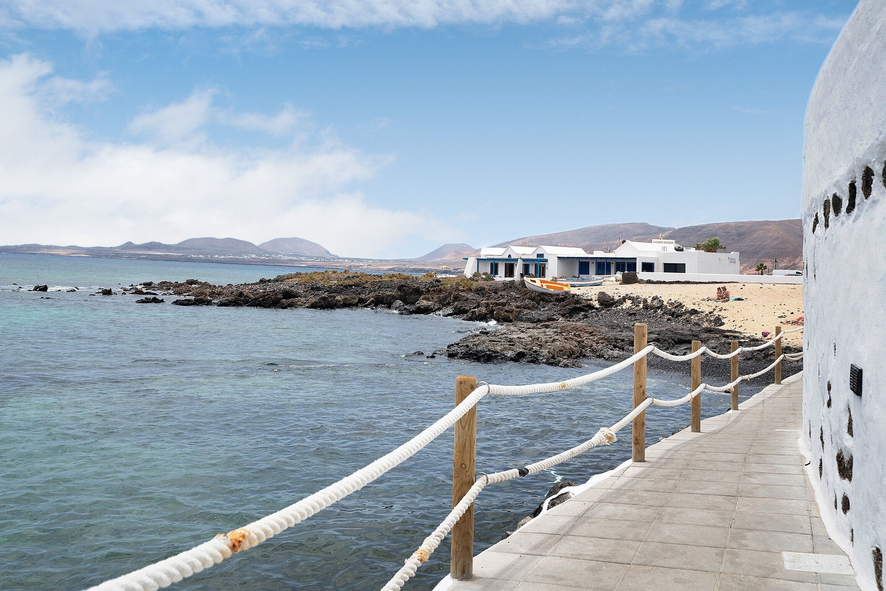 Un passeig marítim que condueix a un edifici amb vista despejada al mar i a muntanyes allunyades.