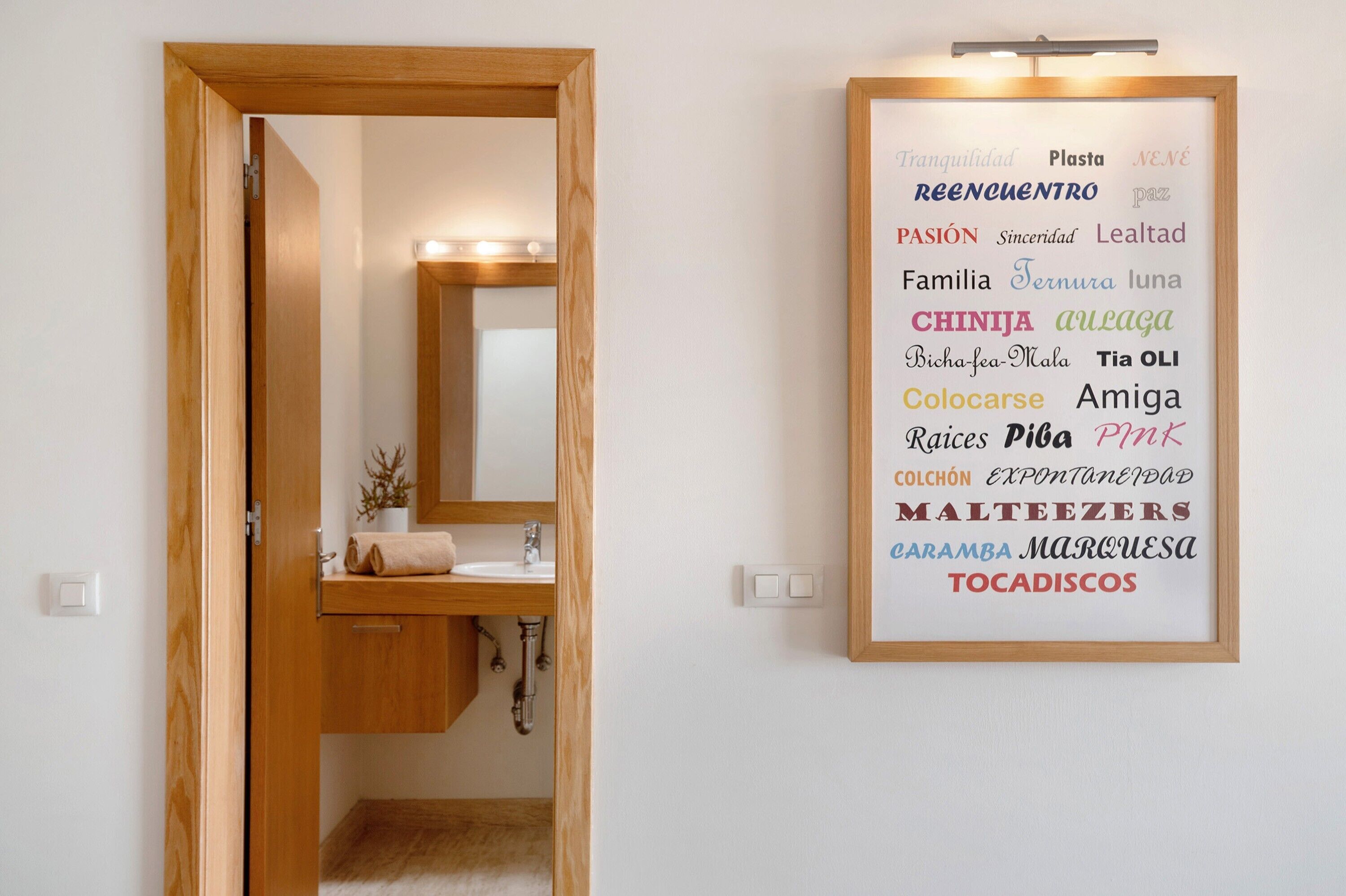 A bathroom with a wooden door, a mirror, a sink, and a wall-mounted light fixture.