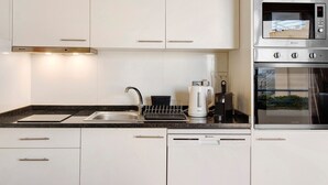Una cocina moderna con armarios blancos, un microondas de acero inoxidable, un horno, una cafetera y un escurreplatos.
