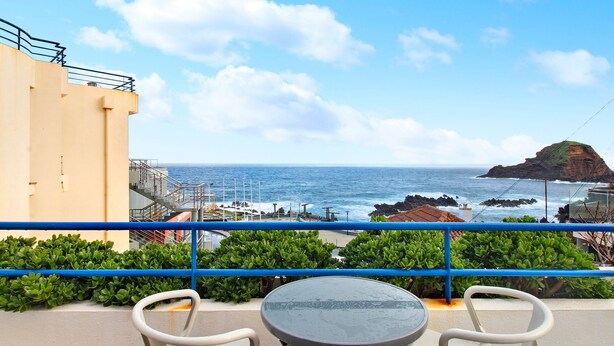 Un balcón con mesa y sillas, con vista al mar y un promontorio rocoso.