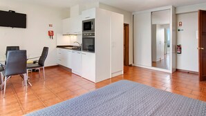 Una cocina moderna con armarios blancos, un microondas y un horno. Hay una mesa de comedor con sillas, una alfombra en el suelo y un extintor de incendios en la pared.