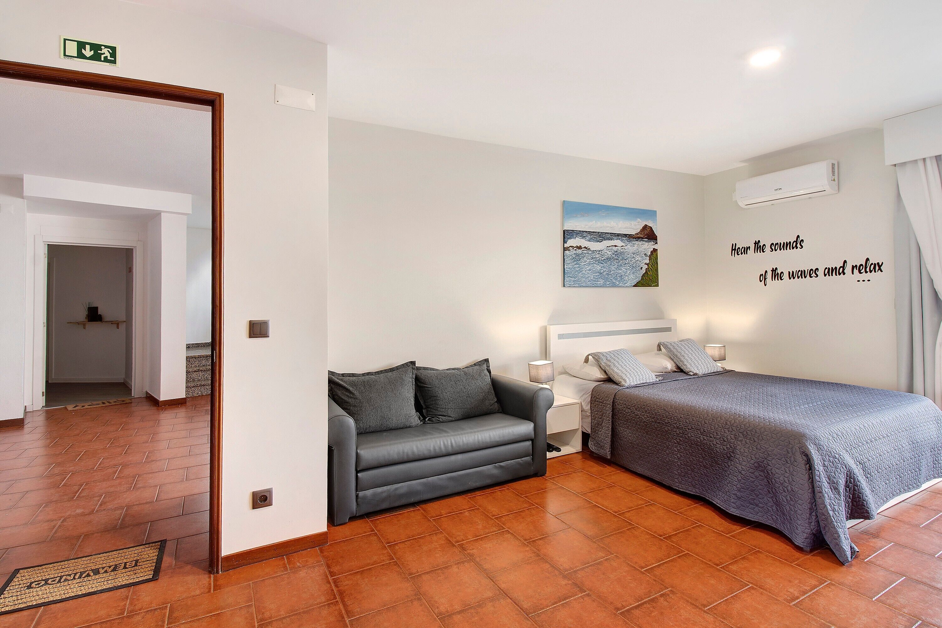 Une pièce comprenant un canapé, un lit, un climatiseur fixé au mur et un tableau.