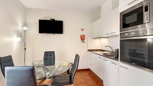 Una cocina compacta con microondas, horno y una mesa de vidrio con sillas.