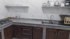A kitchen with granite countertops, dark wooden cabinets, a gas stove, a sink, and various kitchen appliances on the countertop.