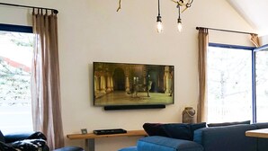 Moderni olohuone, jossa on suuri seinälle asennettu taulutelevisio, sininen sohva, puinen sohvapöytä ja musta nahkainen nojatuoli.