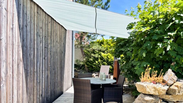 Ulkoterassi, jossa on rottinkihuonekaluja, kiviseinä ja pergola, joka tarjoaa varjoa.
