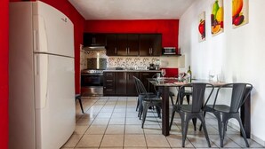 Cocina funcional con refrigerador, estufa y microondas. Se observa una mesa de comedor con sillas y una pared roja.