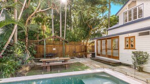 Um quintal com piscina, deck de madeira e área cercada com um banco.