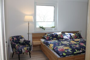 Une chambre à coucher avec un lit en bois, une chaise, une fenêtre avec des stores et une table de chevet.