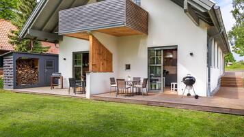 Ein modernes Haus mit überdachter Terrasse, Sitzgelegenheiten im Freien und einer Grillanlage.