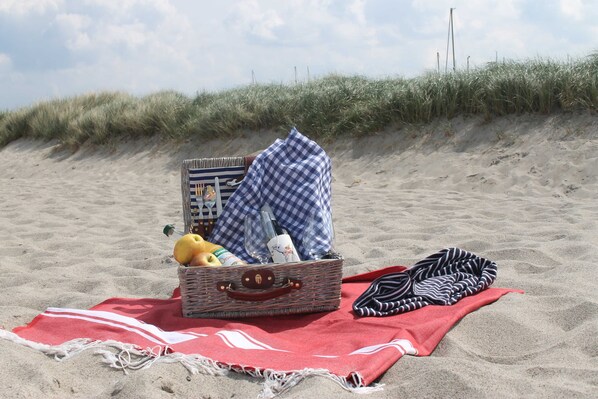 A beach scene with a picnic setup including a basket, blanket, and a bottle. - Ferienwohnung Mond mit Terrasse, Kamin und Garten - Ferienhaus Sonne, Mond und Sterne bei (Steffenshagen)