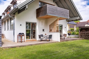 Una casa moderna con terraza, mobiliario exterior y una barbacoa.
