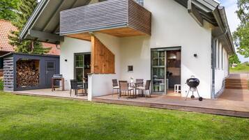 Ein modernes Haus mit überdachter Terrasse, Grill und Holzstapel.