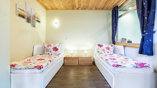 A room with two beds, wooden flooring, a wooden ceiling, and a window with curtains. - Ferienwohnung Mond mit Terrasse, Kamin und Garten - Ferienhaus Sonne, Mond und Sterne bei (Steffenshagen)