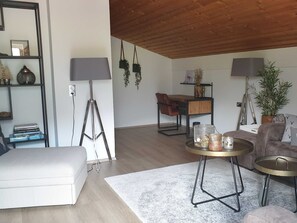 A living room with a sofa, a coffee table, a desk with a chair, and a lamp.