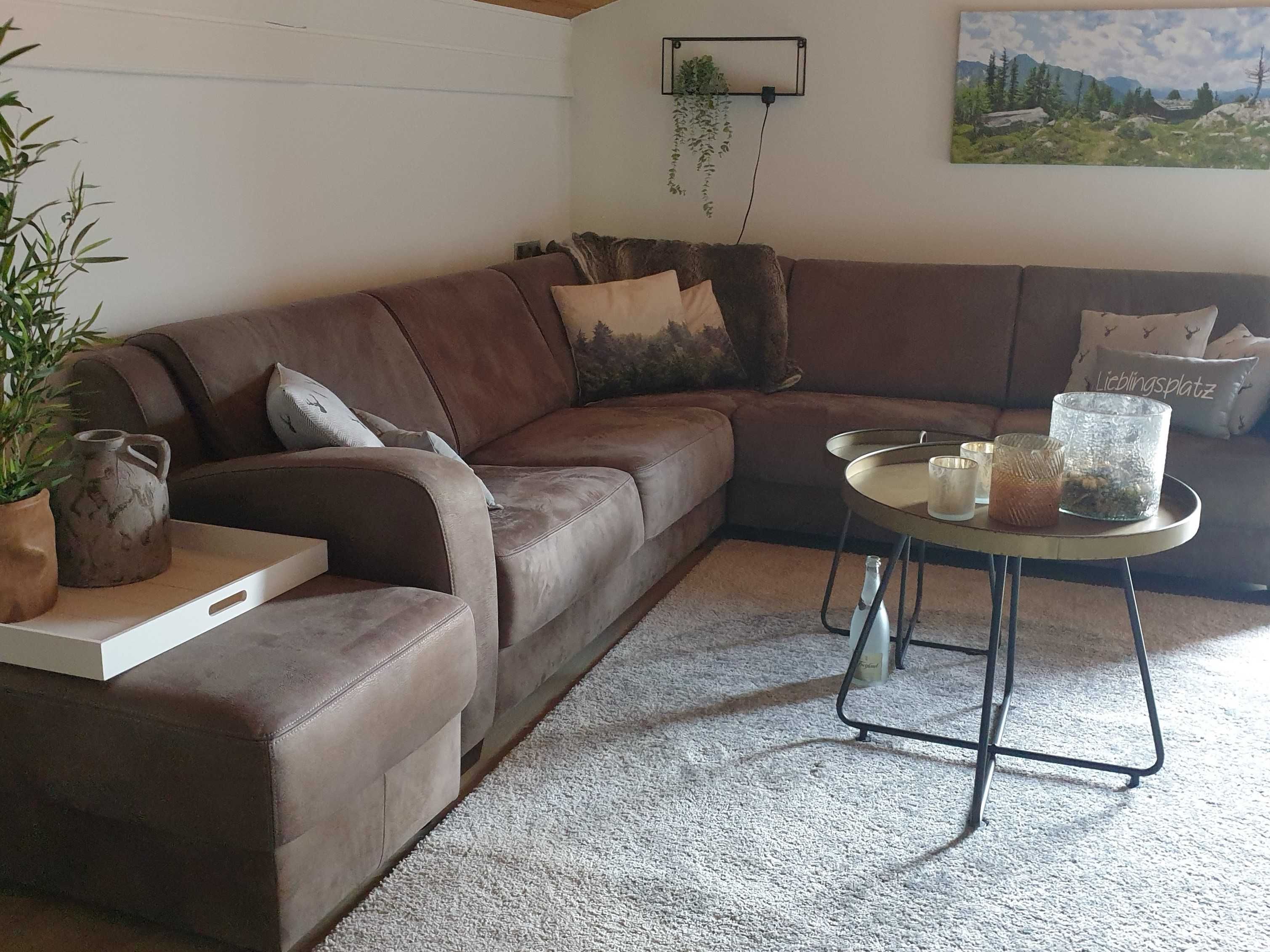 A brown leather sofa with cushions, a small side table with a candle holder, a potted plant, and a wall-mounted plant.