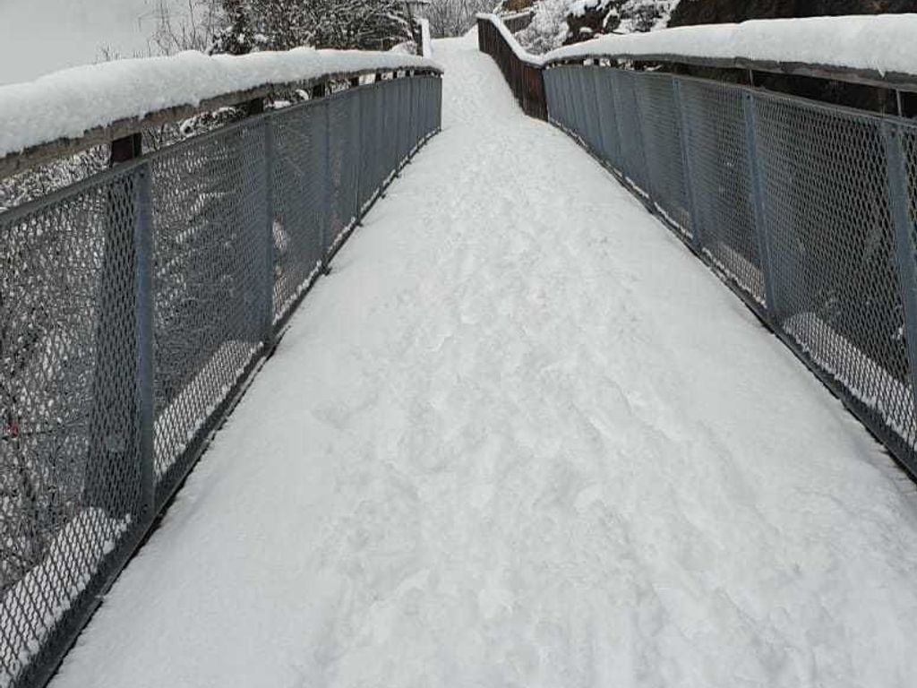 Een sneeuwbedekte voetgangersbrug met metalen hekwerken.
