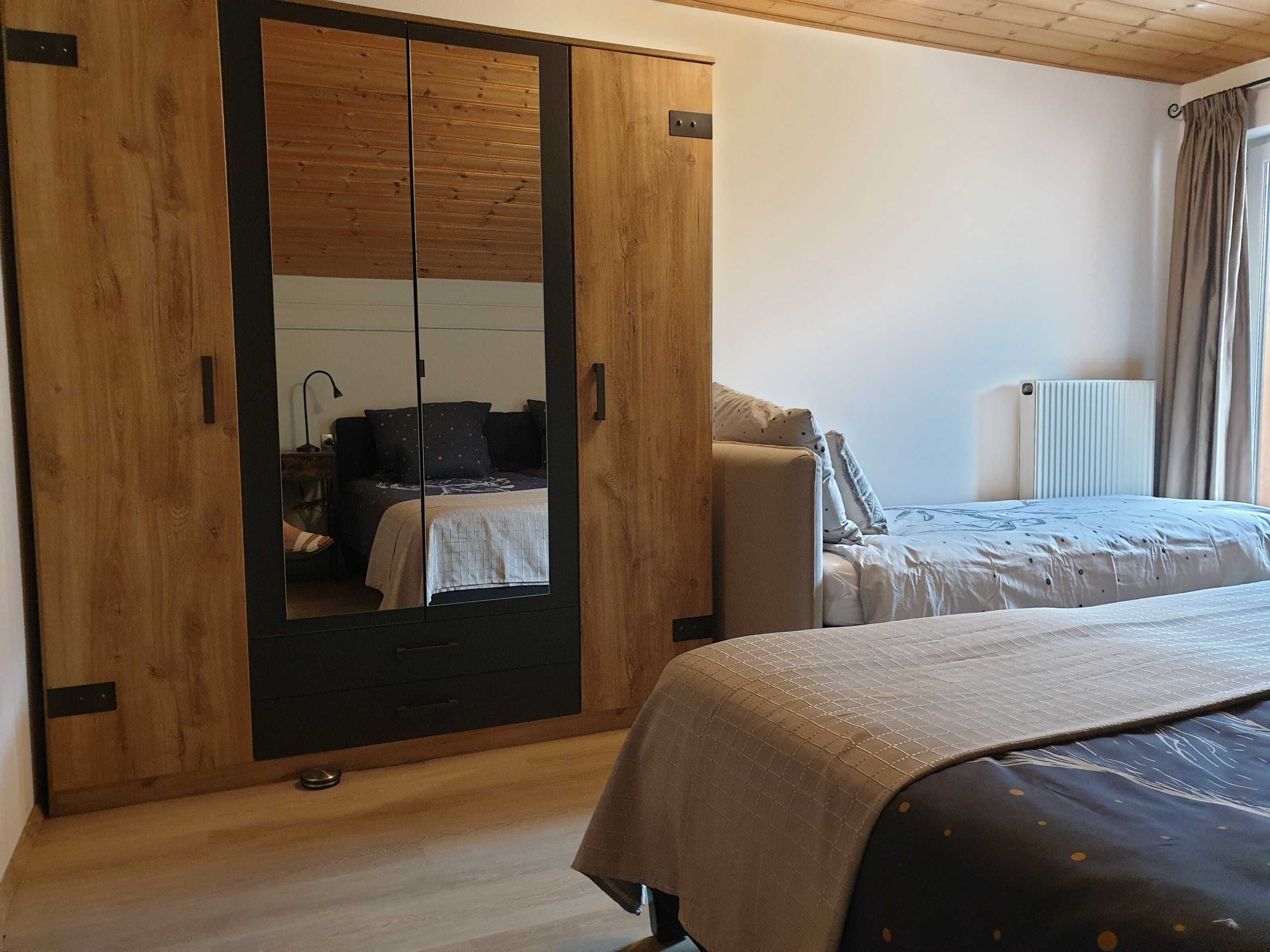 Une chambre avec une armoire en bois, un lit recouvert d’une couette à motifs et un radiateur.