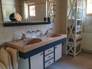 Une salle de bain avec deux lavabos, un miroir, une étagère avec des articles de toilette et un porte-serviettes.