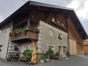 A traditional wooden building with a balcony, potted plants, and a wooden sculpture.